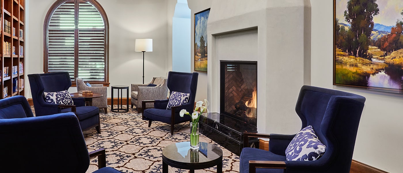 TheGlen-1400x600-5 Blue chairs next to large fireplace in common room at Wisteria