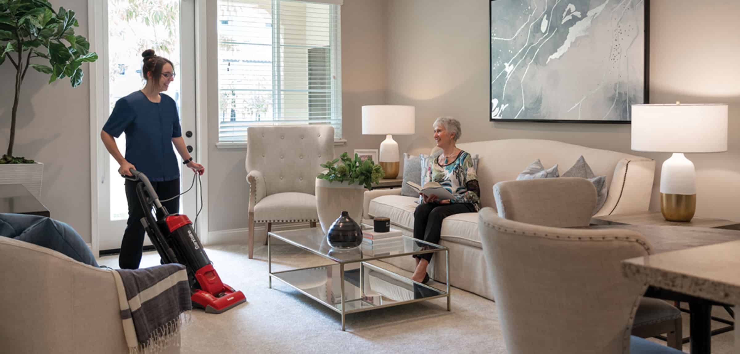 lacosta-2024-600x600-25 A maid vacuuming while a resident is sitting on the couch