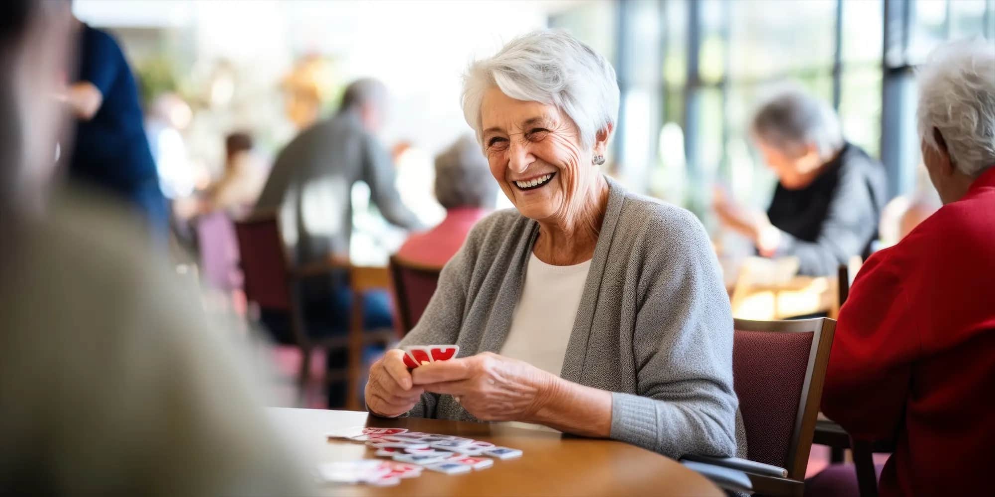 A older women working on a craft with her hands while sitting at a table smiling at a Type-A community